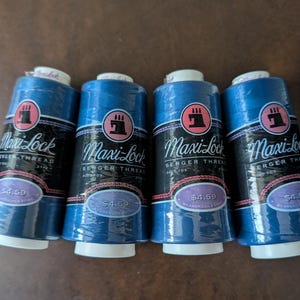 May include: Four spools of blue Maxi-Lock serger thread, each wrapped in clear plastic. The labels feature a black sewing machine icon, the text Maxi-Lock Serger Thread, and a purple oval containing the price of $4.59 and 3000 yards of thread.