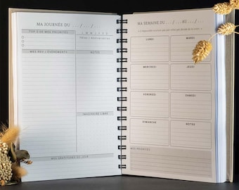 May include: An open spiral-bound planner with white pages featuring black text in French. The left page includes sections for daily priorities, appointments, and gratitude. The right page displays a weekly schedule with daily boxes and a notes section.