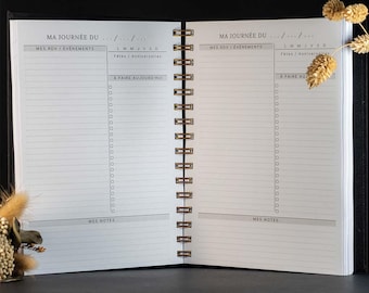 May include: A spiral-bound daily planner open to two pages with white paper and black text. Each page features sections labeled MA JOURNÉE DU, MES RDV / ÉVÉNEMENTS, L M M J V S D, Fêtes / Anniversaires, A FAIRE AUJOURD'HUI with checkboxes, and MES NOTES.