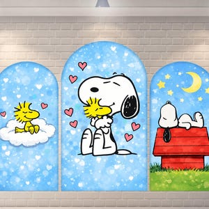 May include: A triptych wall art set featuring Snoopy and Woodstock. The left panel shows yellow Woodstock on a white cloud. The center panel shows white Snoopy hugging yellow Woodstock amidst pink hearts. The right panel shows Snoopy sleeping on a red doghouse under a yellow crescent moon.