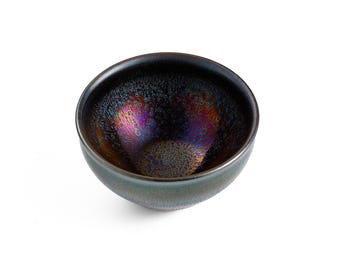 Puede incluir: Un pequeño cuenco de cerámica oscura con un esmalte irisado moteado. El esmalte tiene un color profundo y rico con toques de morado, azul y dorado.