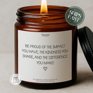 Op de afbeelding: Een brandende sojawas kaars in een bruine glazen pot met een zwart deksel. Op het etiket staat "Wees trots op de impact die je hebt, de vriendelijkheid die je deelt en het verschil dat je maakt!" met een hart symbool. De kaars is 113 gram.