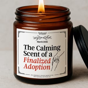Könnte beinhalten: Eine brennende Kerze in einem bernsteinfarbenen Glas mit schwarzem Deckel. Das Etikett lautet "The Calming Scent of a Finalized Adoption" mit dem Text "March 2026" und "Firebound by Valenti". Die Kerze besteht aus 100% natürlichem Sojawachs und wiegt 113g.