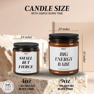 May include: Two brown glass jar candles with black lids. The smaller candle is 2.4 inches tall and reads "SMALL BUT FIERCE". The larger candle is 3.5 inches tall and reads "BIG ENERGY BABE". The candles are on a stone surface.