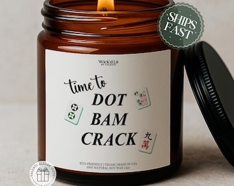 Könnte beinhalten: Eine brennende Kerze in einem bernsteinfarbenen Glas mit schwarzem Deckel. Das weiße Etikett zeigt den Text "Wick'd Lit BY VALENTI", "time to DOT BAM CRACK" und "ECO-FRIENDLY | VEGAN | MADE IN USA 100% NATURAL SOY WAX | 113g" sowie drei Mahjong-Steine.