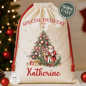 May include: A cream-colored Christmas gift bag with red drawstrings and trim. The bag features a festive illustration of Santa Claus, a decorated Christmas tree, and the words "Special Delivery For Katherine".