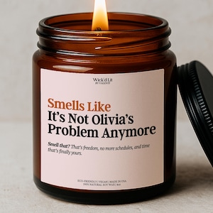 May include: A lit soy wax candle in a brown glass jar with a black lid. The label reads "Smells Like It's Not Olivia's Problem Anymore." The candle is eco-friendly, vegan, and made in the USA. It contains 4 oz of natural soy wax.