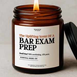 May include: A lit soy wax candle in a brown glass jar with a black lid. The label reads "The Uplifting Scent OF A BAR EXAM PREP." The text below says "Smell that? 90% overthinking, 10% panic. SURVIVAL MODE: ON."