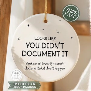 May include: A white ceramic ornament with the text "LOOKS LIKE YOU DIDN'T DOCUMENT IT" in black. The ornament has a gold string for hanging and is decorated with small star shapes. A green sticker says "SHIPS FAST".