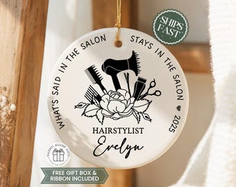 May include: A round white ceramic ornament featuring a black graphic of a hair dryer, comb, shears, and a rose. The text reads: WHAT'S SAID IN THE SALON STAYS IN THE SALON, HAIRSTYLIST, and the name Evelyn with the year 2025 and a small heart.