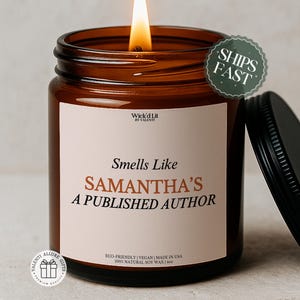 Könnte beinhalten: Eine brennende Kerze in einem braunen Glas mit schwarzem Deckel. Auf dem Etikett steht "Smells Like Samantha's A Published Author". Die Kerze ist umweltfreundlich, vegan und in den USA hergestellt.