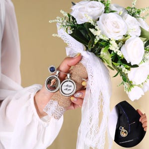 May include: A bridal bouquet with white roses and greenery, held with a burlap-wrapped handle. Two round photo charms with the text "Always with you" are pinned to the bouquet, along with a blue gemstone ring.