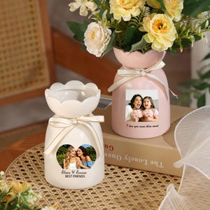 May include: Two ceramic vases with scalloped rims and cream-colored ribbons. The white vase features a heart-shaped photo of two people with the text Elara & Emma BEST FRIENDS. The pink vase displays a rectangular photo with the text I love you more than word.