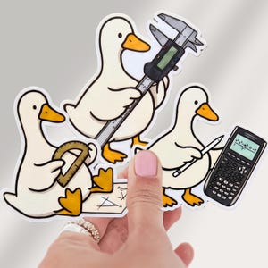 May include: Three white cartoon ducks with orange beaks and feet. One duck holds a digital caliper, another holds a protractor over a geometric drawing, and the third holds a white pencil next to a black scientific calculator with a screen display.