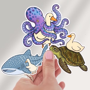 May include: Three die-cut vinyl stickers featuring cartoon animals. One shows a purple octopus hugging a white duck, another a blue whale shark with a small white duck, and the third a green sea turtle with a white duck perched on its shell.
