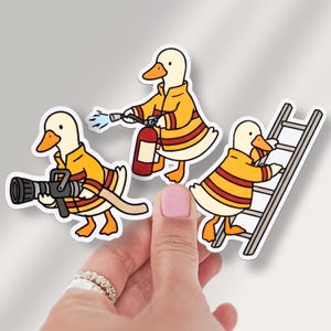 May include: Three stickers featuring cartoon ducks dressed as firefighters. One duck holds a fire hose, another a fire extinguisher, and the third climbs a ladder. The ducks wear yellow and red striped uniforms.
