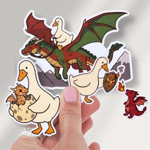 May include: A collection of die-cut vinyl stickers featuring white ducks and dragons. One sticker shows a duck riding a green dragon, another shows a duck with a baby dragon in an egg, and others show a duck with a shield and a small red dragon.