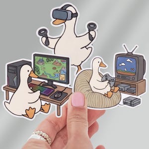 May include: Three die-cut stickers featuring white ducks in gaming scenarios. One duck wears a VR headset with controllers, another sits at a computer desk with a rainbow keyboard, and the third sits in a beanbag chair playing a retro console game.