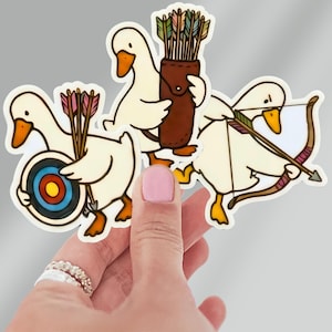 May include: A collection of die-cut stickers featuring cartoon geese in archery poses. One goose holds a bow and arrow, another a target, and a third carries a quiver of arrows. The geese are white with orange beaks and feet, and the arrows have colorful fletching.