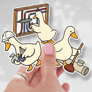 May include: A set of three stickers featuring cartoon ducks in various plumbing-related roles. One duck wears a hard hat and holds tools, another works on pipes, and the third holds a plunger and pipe. The stickers have a white border.