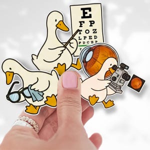 May include: A set of whimsical stickers featuring cartoon ducks in various ophthalmology-related scenarios. One duck points to an eye chart, another holds glasses and a cloth, and a third examines an eye with a machine.
