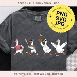 May include: Dark gray long-sleeve shirt featuring a baseball-themed design with cartoon geese. The geese are depicted in various baseball positions, wearing hats and sunglasses. A yellow circle with text is in the upper right corner.