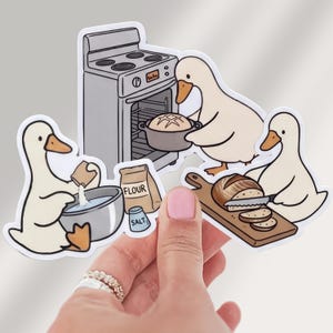 May include: A die-cut sticker featuring three white ducks baking bread. One duck pours ingredients into a bowl, another places a pot into a gray oven, and the third slices a loaf of bread on a wooden board. A bag labeled FLOUR and a shaker labeled SALT are included.