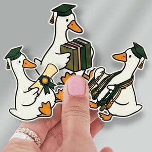 May include: Three stickers featuring cartoon geese in graduation caps. One goose holds a diploma, another holds books, and the third wears a graduation stole. The geese are white with orange beaks and feet, and the caps are green.