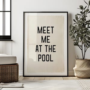 May include: A rectangular wall art print in a black frame featuring the black text MEET ME AT THE POOL centred on a light beige, textured fabric background with frayed edges, displayed in a vertical orientation for wall decor.