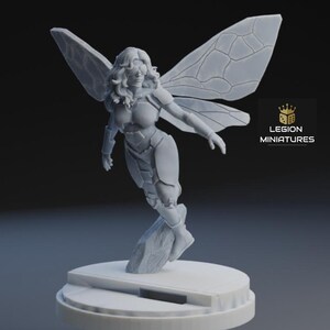Op de afbeelding: Een grijze miniatuurfiguur van een vrouw met insectenachtige vleugels, gekleed in een nauwsluitend pak en een bril. De figuur is in vlucht geposeerd, gemonteerd op een cirkelvormige basis. Het Legion Miniatures logo is zichtbaar.