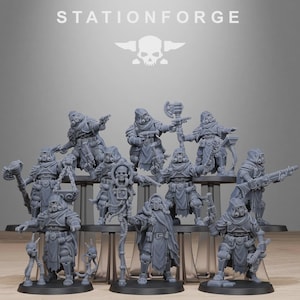 May include: A group of grey miniature figures, possibly for tabletop gaming, displayed on a tiered stand. The figures are detailed with gas masks, armour, and weapons. The text "STATIONFORGE" and a skull logo are visible at the top.