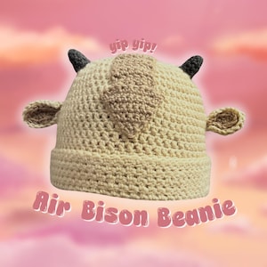 Könnte beinhalten: Eine gehäkelte beige Mütze mit braunen Ohren und einem braunen Fleck auf der Oberseite. Die Mütze trägt den Text "yip yip!" darüber und "Air Bison Beanie" darunter.
