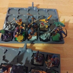 Peut inclure: Un plateau de rangement en plastique gris avec 16 compartiments, chacun contenant une figurine miniature peinte de diff&eacute;rentes couleurs. Les figurines sont habill&eacute;es de costumes diff&eacute;rents et tiennent des armes et des outils.