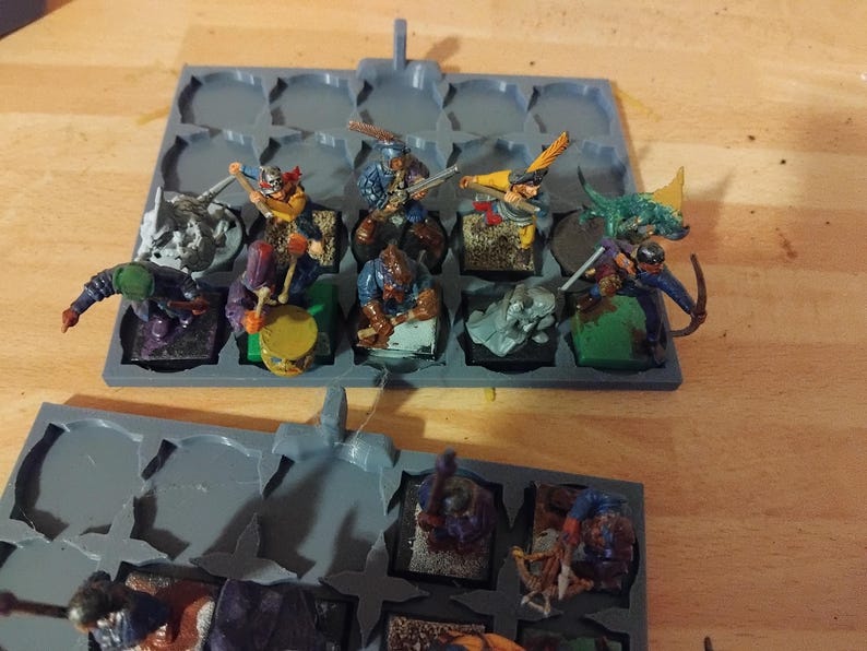 Peut inclure: Un plateau de rangement en plastique gris avec 16 compartiments, chacun contenant une figurine miniature peinte de diff&eacute;rentes couleurs. Les figurines sont habill&eacute;es de costumes diff&eacute;rents et tiennent des armes et des outils.