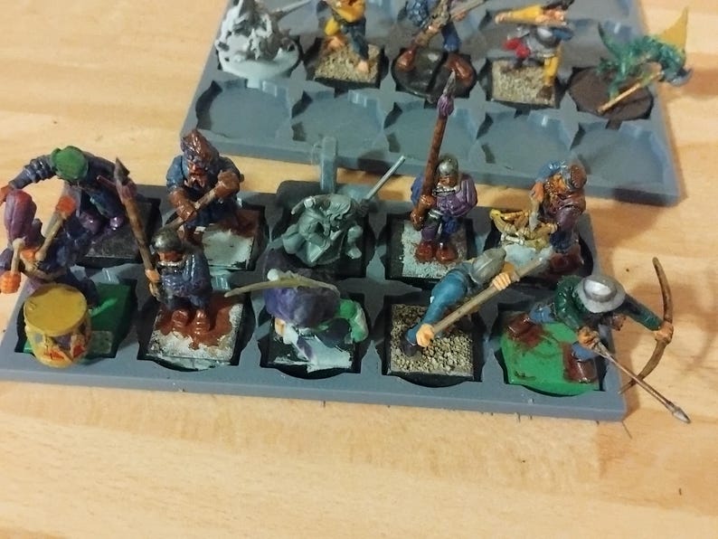 Peut inclure: Un ensemble de dix figurines miniatures, peintes dans diff&eacute;rentes couleurs, sont expos&eacute;es sur une base en plastique grise. Les figurines sont dispos&eacute;es en grille, chaque figurine &eacute;tant sur un carr&eacute; s&eacute;par&eacute;. Les figurines portent toutes des costumes diff&eacute;rents et tiennent diverses armes et accessoires.