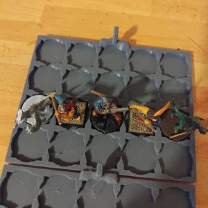Peut inclure: Une bo&icirc;te de rangement en plastique gris avec 16 compartiments circulaires pour ranger des figurines miniatures. La bo&icirc;te est ouverte et montre quatre figurines miniatures dans diff&eacute;rentes poses. Les figurines sont peintes dans diff&eacute;rentes couleurs, notamment le gris, le brun, le jaune et le vert.