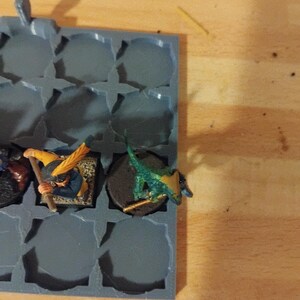 Peut inclure: Un plateau de rangement en plastique gris avec des compartiments circulaires, contenant des figurines miniatures peintes en vert, jaune et bleu.