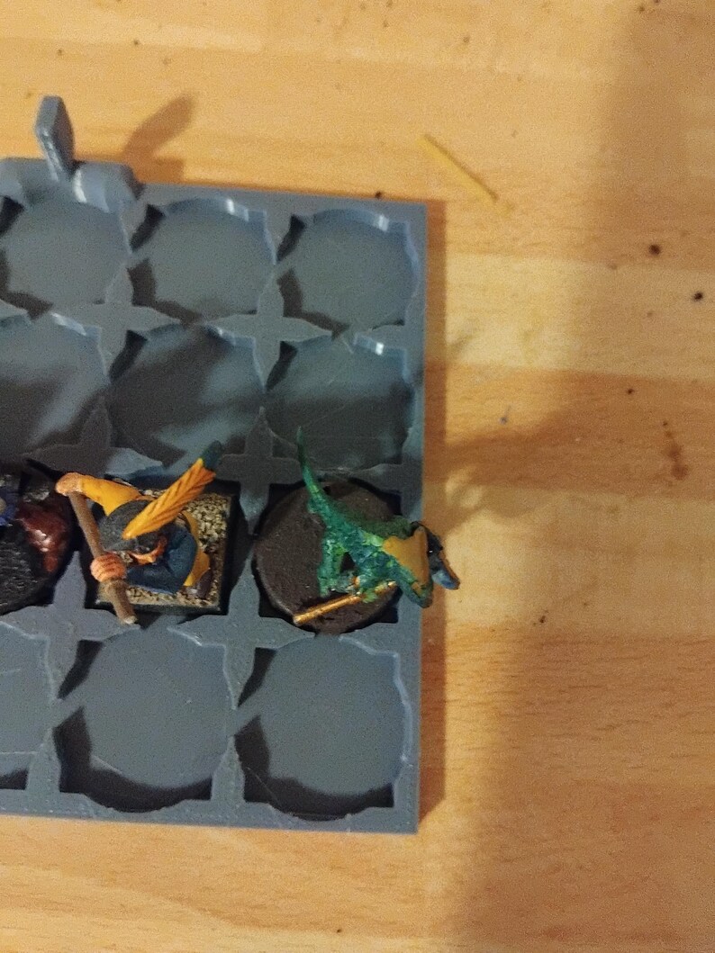 Peut inclure: Un plateau de rangement en plastique gris avec des compartiments circulaires, contenant des figurines miniatures peintes en vert, jaune et bleu.