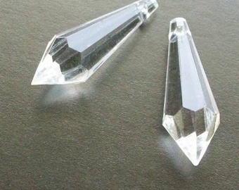 May include: Two clear glass crystal teardrop shaped pendants. The pendants are faceted and have a pointed tip.