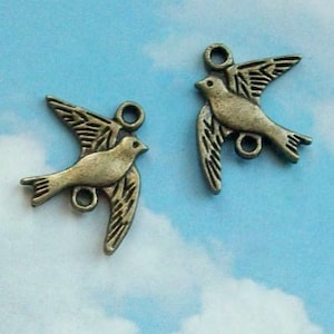 May include: Two antique bronze bird charms with a loop for hanging. The birds are in flight with their wings spread.