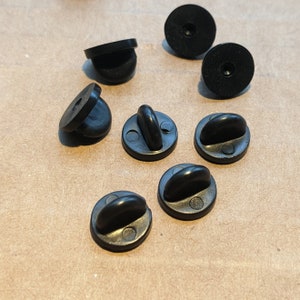 May include: Eight black plastic pin back closures for crafts and DIY projects. The closures are round and have a small pin on the back.