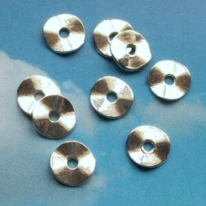 May include: A set of eight silver-toned metal spacer beads. Each bead is a flat disc with a hole in the center. The beads are perfect for adding a touch of sparkle to jewelry projects.