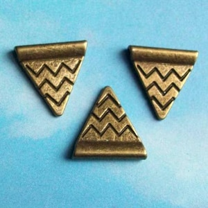May include: Three antique gold-toned metal triangle-shaped charms with a chevron pattern.