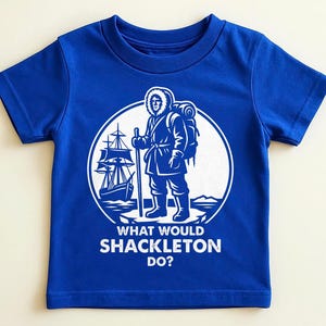 May include: Royal blue t-shirt with a white graphic. The graphic shows a person with a backpack, a sailing ship, and the text "WHAT WOULD SHACKLETON DO?" inside a white circle.