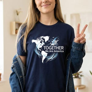 Puede incluir: Camiseta azul marino con un gr&aacute;fico de mapa del mundo blanco y el texto "TOGETHER We Are America". El dise&ntilde;o incluye remolinos azules y un p&aacute;jaro estilizado. La camiseta es de manga corta.