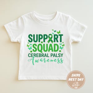 Op de afbeelding: Wit T-shirt met een groen en blauwgroen ontwerp. Het shirt heeft de woorden "SUPPORT SQUAD" en "CEREBRAL PALSY Awareness" met vlindergraphics. Een groen lint is ook inbegrepen.