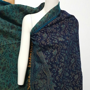 Op de afbeelding: Een blauwe en groene gestreepte sjaal met een gouden franje. De sjaal is gemaakt van een zachte, lichte stof en is perfect om elke outfit een vleugje elegantie te geven.