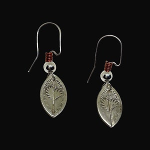 May include: Silver earrings with a leaf-shaped design featuring a United States coin with the words "United States of America" and a tree design. The earrings have a copper wire accent.