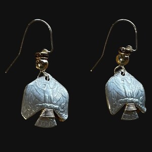 May include: Silver eagle coin earrings with gold accents. The coins are cut in half and shaped into a bird. The earrings are hanging from gold hooks.