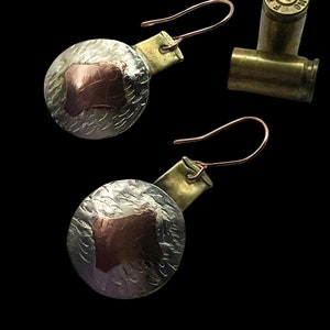 Puede incluir: Un par de pendientes de plata y cobre con textura martillada y un cuadrado de cobre en el centro. Los pendientes cuelgan de un gancho de latón.